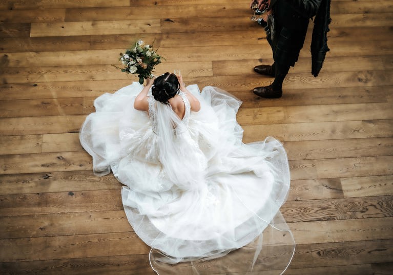 View from above of bride holding bouquet and sitting on wooden floor